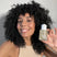 Woman with dark, curly hair smiling holding Act+Acre Stem Cell Scalp Serum