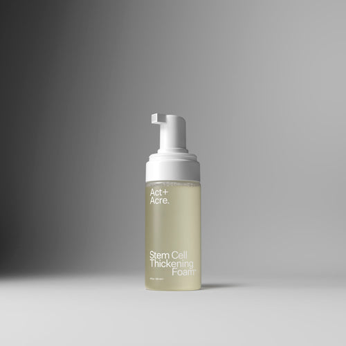 A bottle of Act+A. Stem Cell Thickening Foam with a white pump dispenser and a frosted clear bottle showing a pale yellow-green liquid, set against a clean gray gradient background.