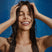 Woman washing her hair under a shower with a blue background