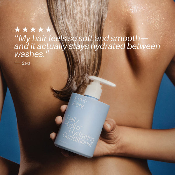 Person holding a bottle of Act+Acre Daily Hydro™ Hydrating Conditioner with a blue background.