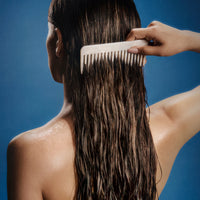 Person combing wet hair against a blue background